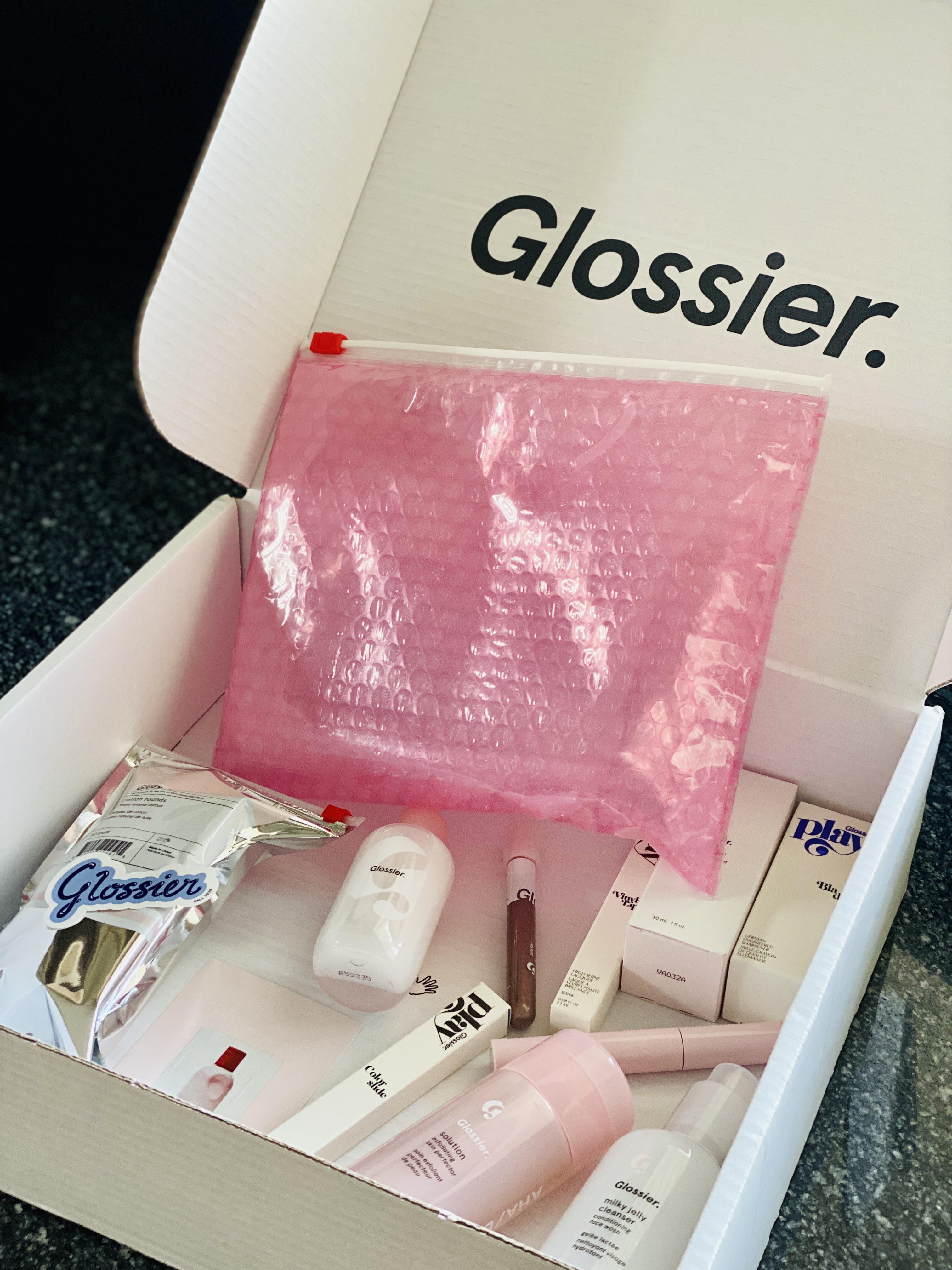 Glossier clean white mailer box opening to reveal the signature pink bubble wrap pouch