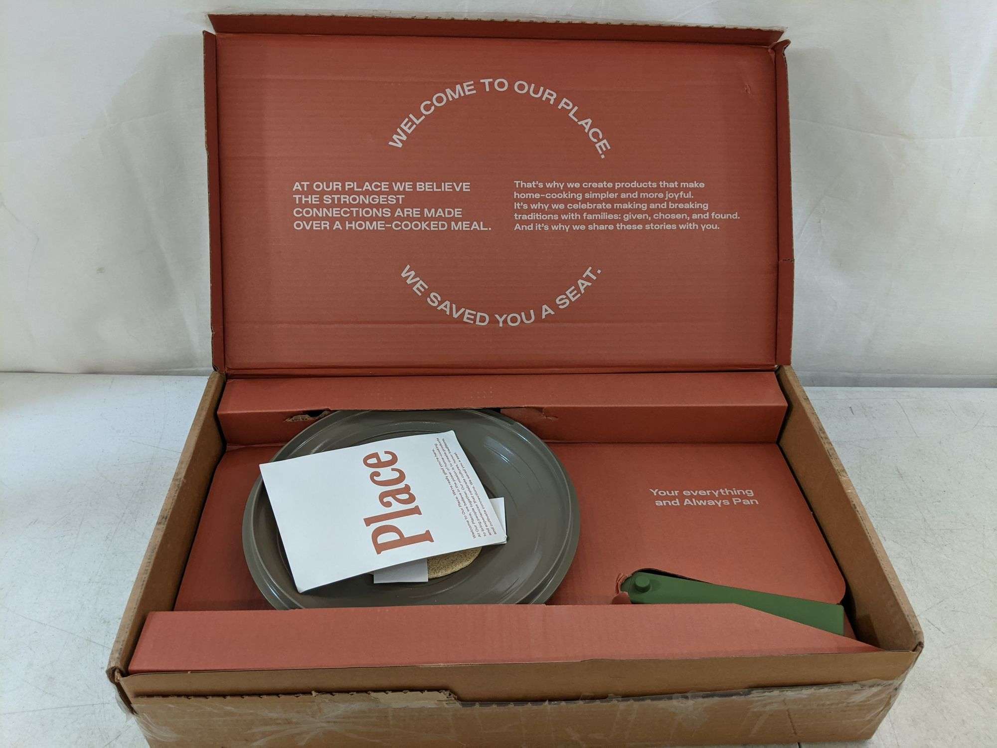 Our Place plain corrugated exterior opening to fully printed terracotta interior with brand manifesto and We saved you a seat